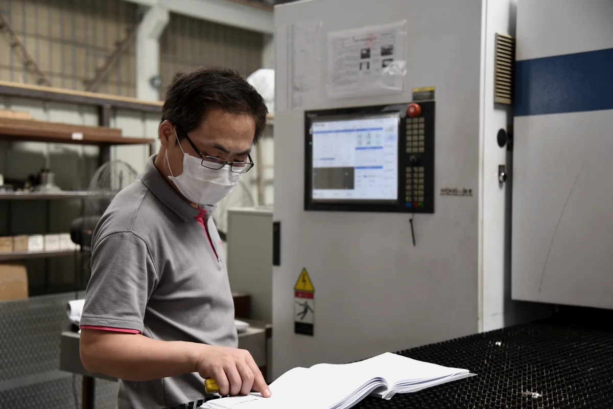 Un ingénieur examine les plans d'enceinte à côté d'un équipement de fabrication de tôlerie.